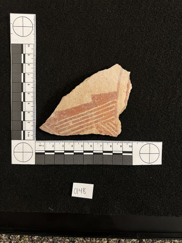 A pottery sherd on a black background with a measurement reference