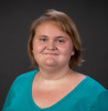 Woman with shoulder length light brown hair wearing a teal colored, v-neck top. 