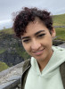 Woman with short or pulled back curly black hair wearing a light green sweatshirt. Rolling green hillside in the background. 